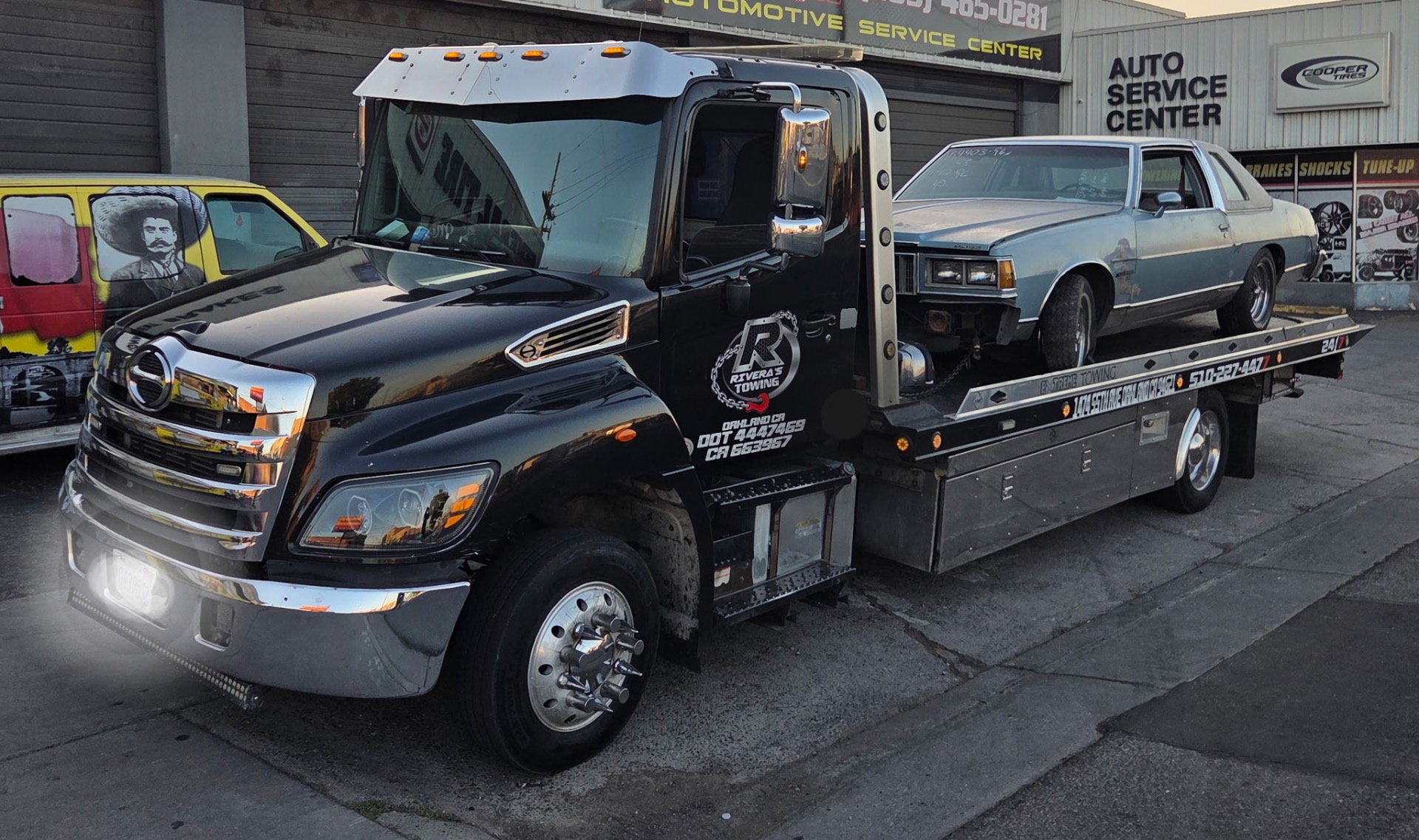 Rivera's Towing black flatbed with classic Pontiac coupe loaded outside Oakland auto service center